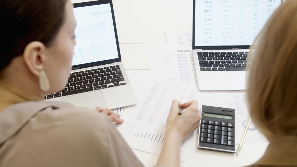 Two people analyzing business data on laptops with charts and graphs. services de travel planner