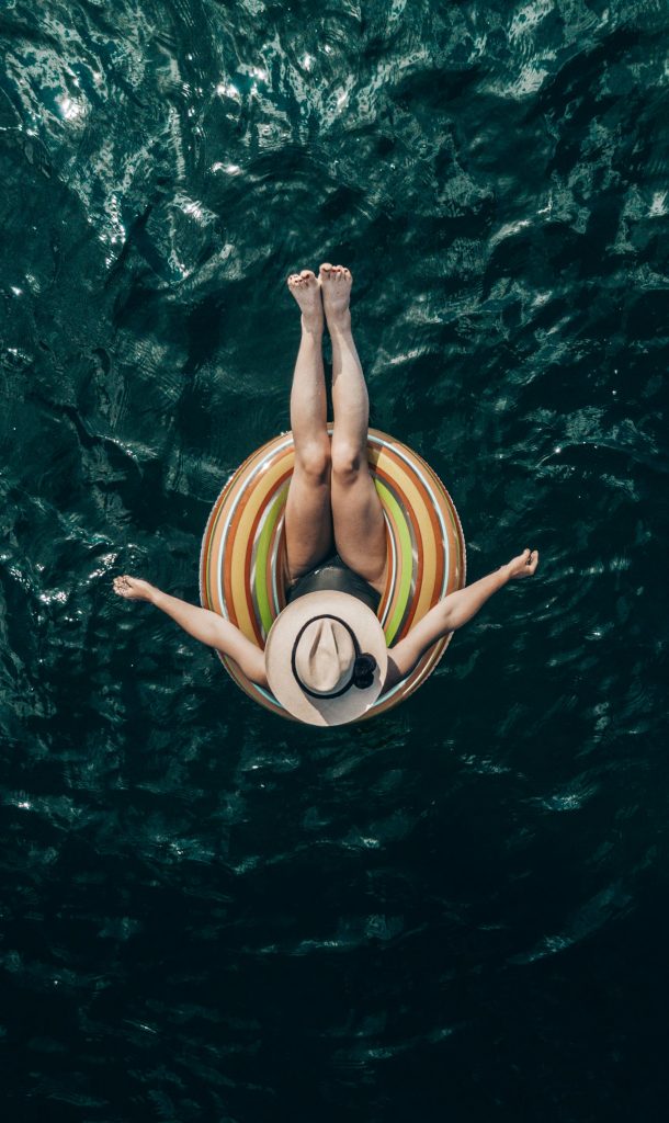 Top view of unrecognizable barefoot tourist in hat lying in inflatable ring on rippled sea travel planner personnalisé