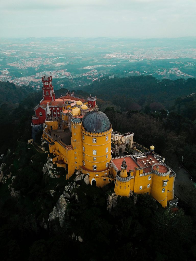 tunning aerial shot of the colorful Pena Palace amidst lush greenery in Sintra, Portugal.