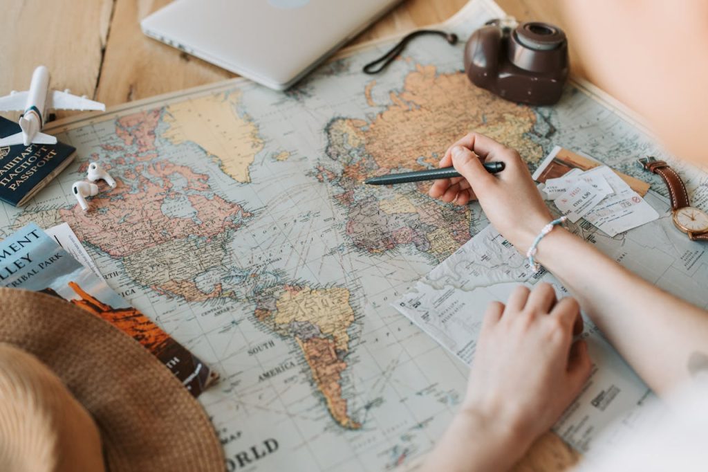Hands marking destinations on a world map surrounded by travel essentials like passport and camera. services de travel planner