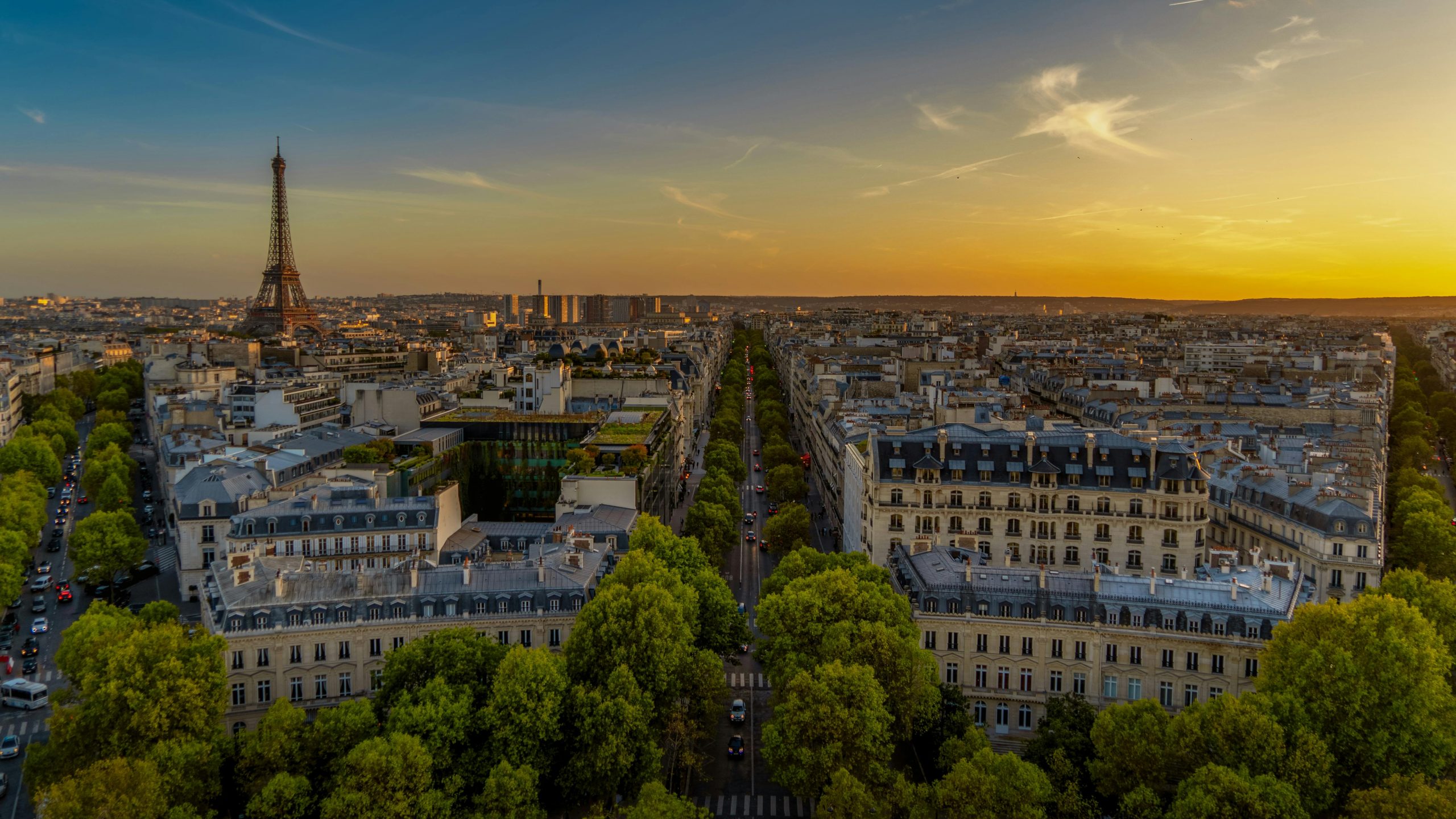 Vivid sunset sky over Arc de Triomphe, capturing Parisian traffic and architecture.