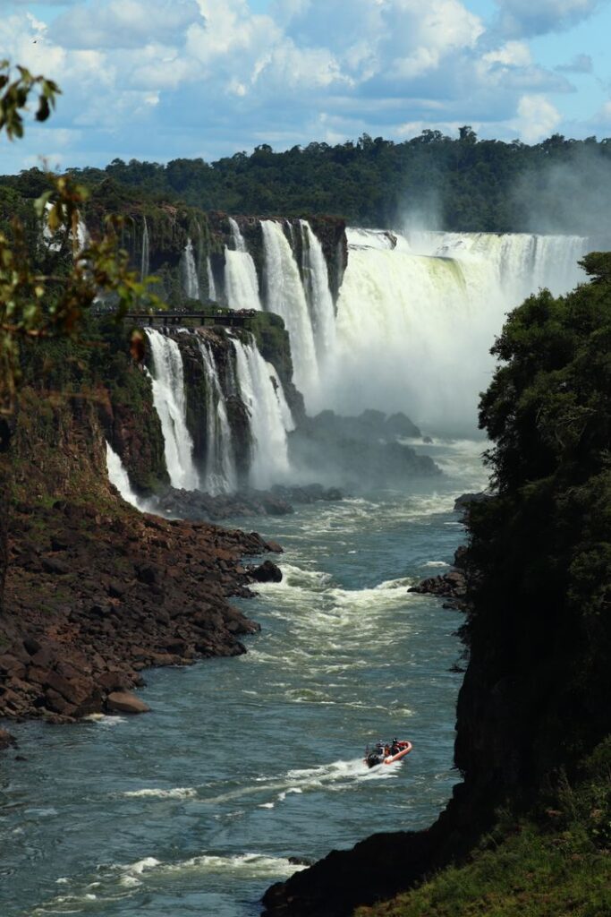 Scenic view of Iguazu Falls with a boat navigating the river below, surrounded by lush greenery.