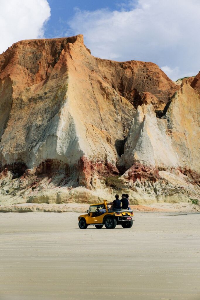pexels-photo-27036126-27036126 Couple in a yellow vehicle enjoys a serene beach drive with stunning cliffs.
