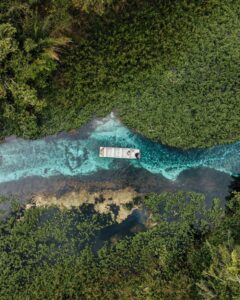 Drone captures a boat on vibrant blue waters surrounded by lush greenery in Bonito, Brazil, showcasing nature's beauty.