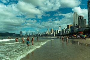 Vibrant beach scene with people enjoying the sun, skyscrapers, and ocean waves.